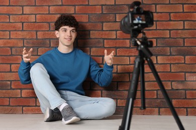 Photo of Smiling teenage blogger explaining something while streaming indoors