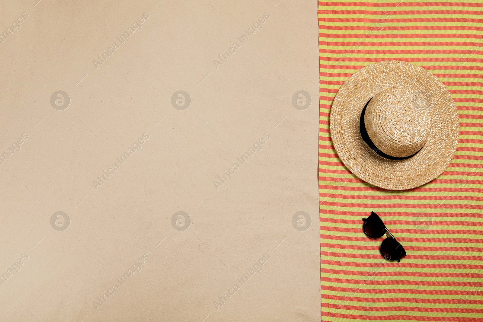 Photo of Striped beach towel, hat and sunglasses on sand, top view. Space for text