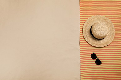 Striped beach towel, hat and sunglasses on sand, top view. Space for text