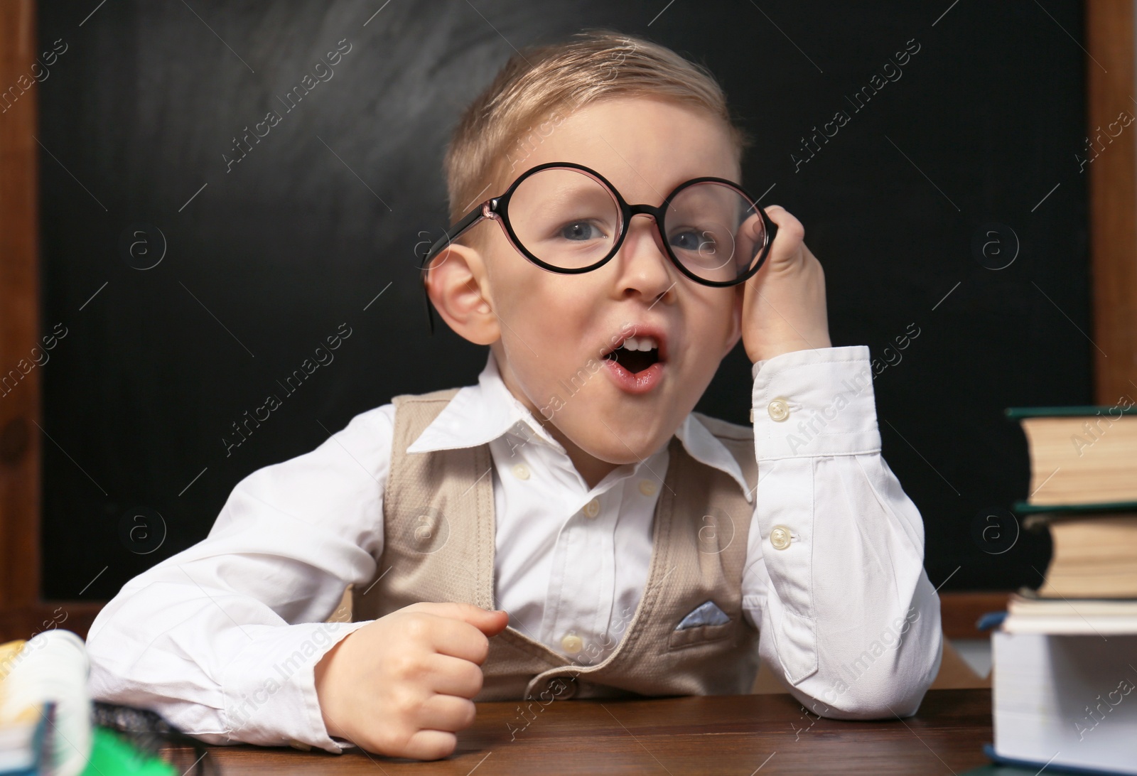 Photo of Cute little child wearing glasses at desk in classroom. First time at school