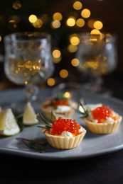 Delicious tartlets with red caviar, cream cheese and lemon served near wine on black table, closeup. Space for text