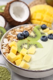 Photo of Tasty matcha smoothie bowl served with fresh fruits and oatmeal on table, closeup. Healthy breakfast