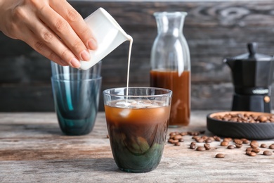 Woman pouring milk into glass with cold brew coffee on table