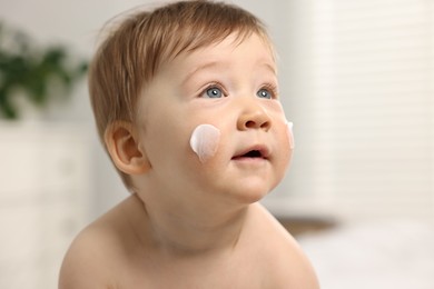 Photo of Cute little baby with moisturizing cream on face indoors