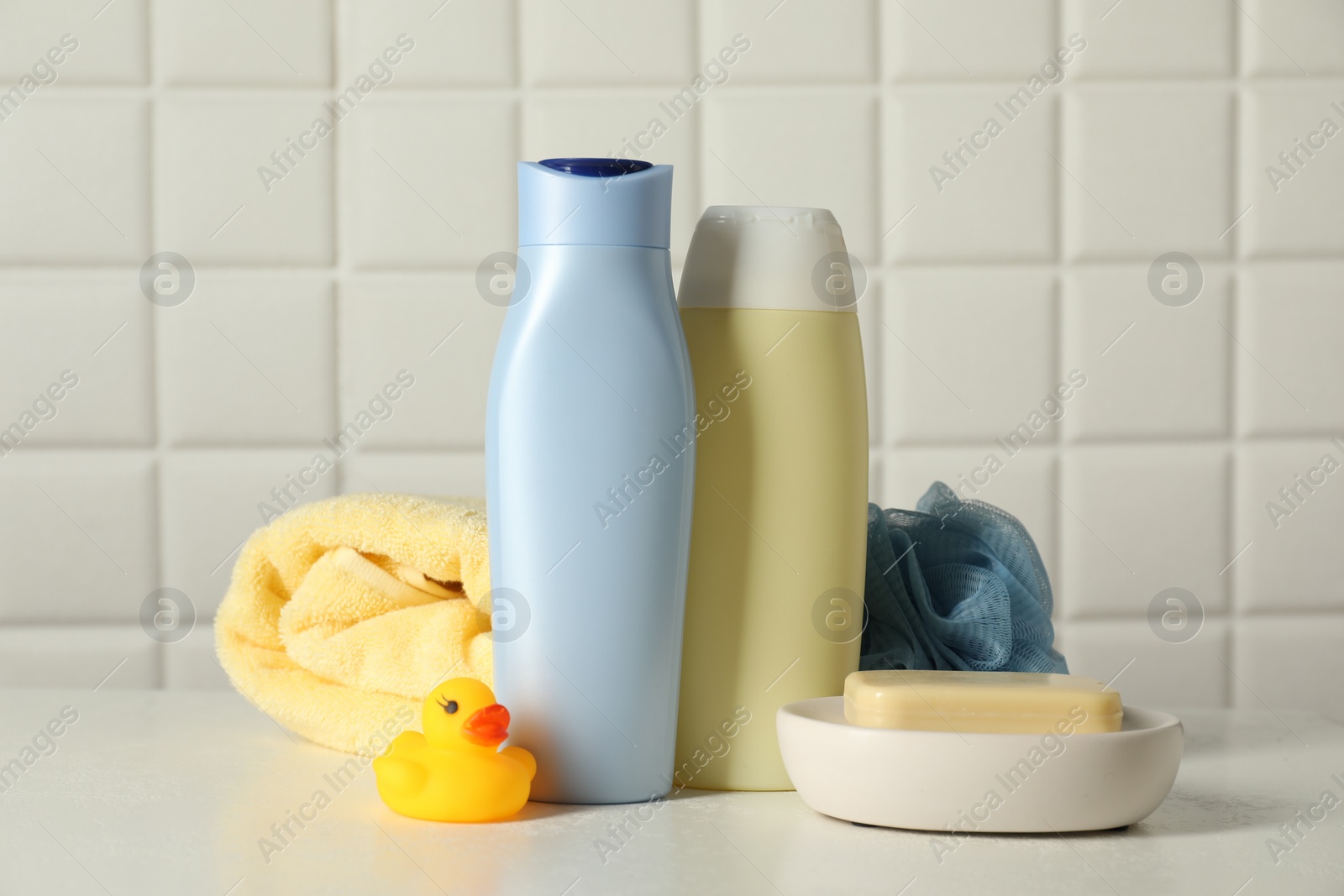 Photo of Baby cosmetic products, bath duck, sponge and towel on white table against tiled wall