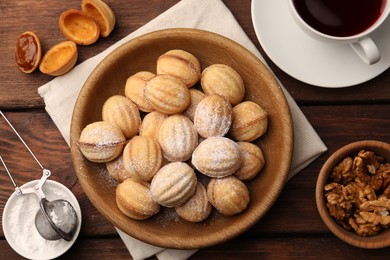 Photo of Delicious nut shaped cookies with boiled condensed milk and powdered sugar on wooden table, flat lay