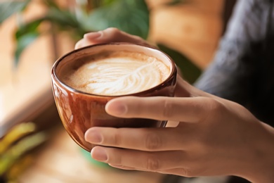Photo of Woman holding cup of aromatic coffee with foam, closeup
