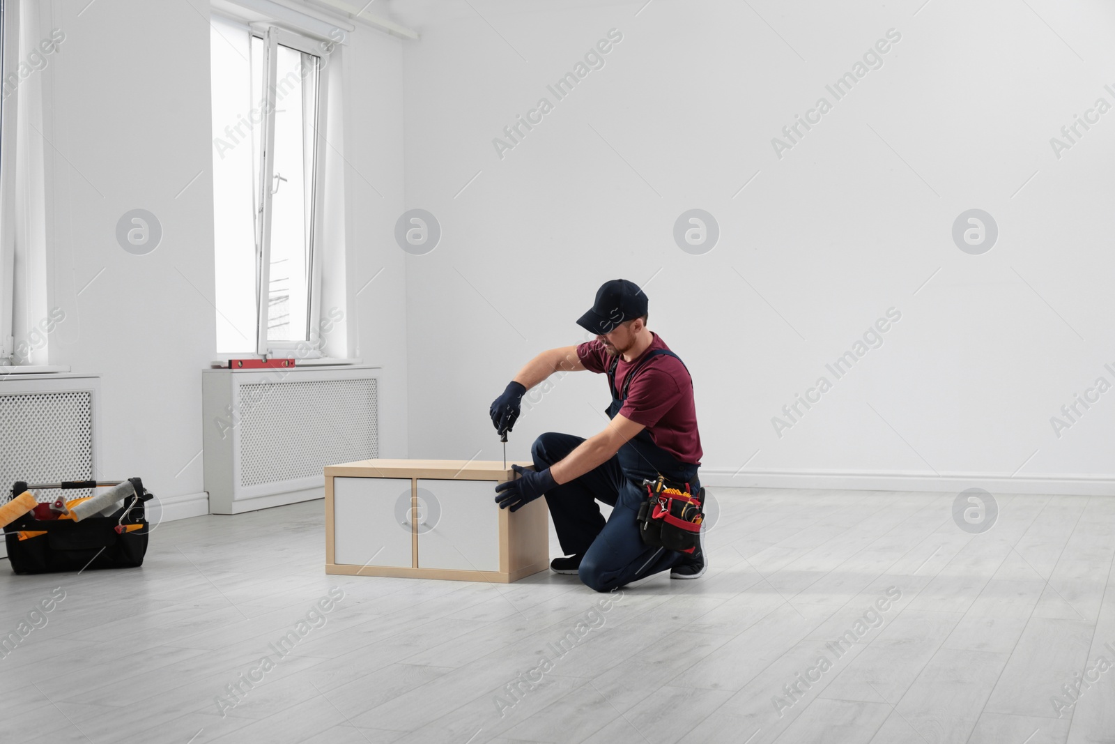 Photo of Handyman in uniform assembling furniture indoors. Professional construction tools