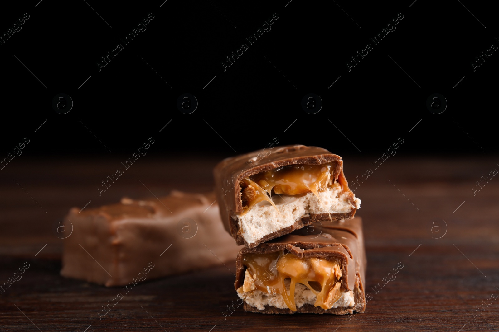 Photo of Chocolate bars with caramel, nuts and nougat on wooden table, closeup