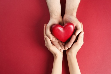 Photo of Couple holding decorative heart on color background, top view