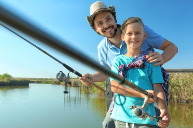 Photo of Father and son fishing together on sunny day. Space for text