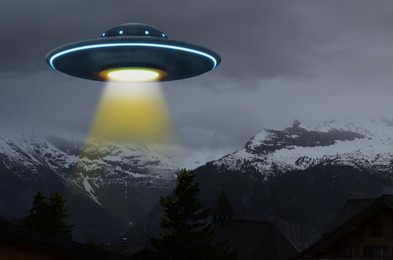 Image of Alien spaceship emitting light beam in air over mountains. UFO