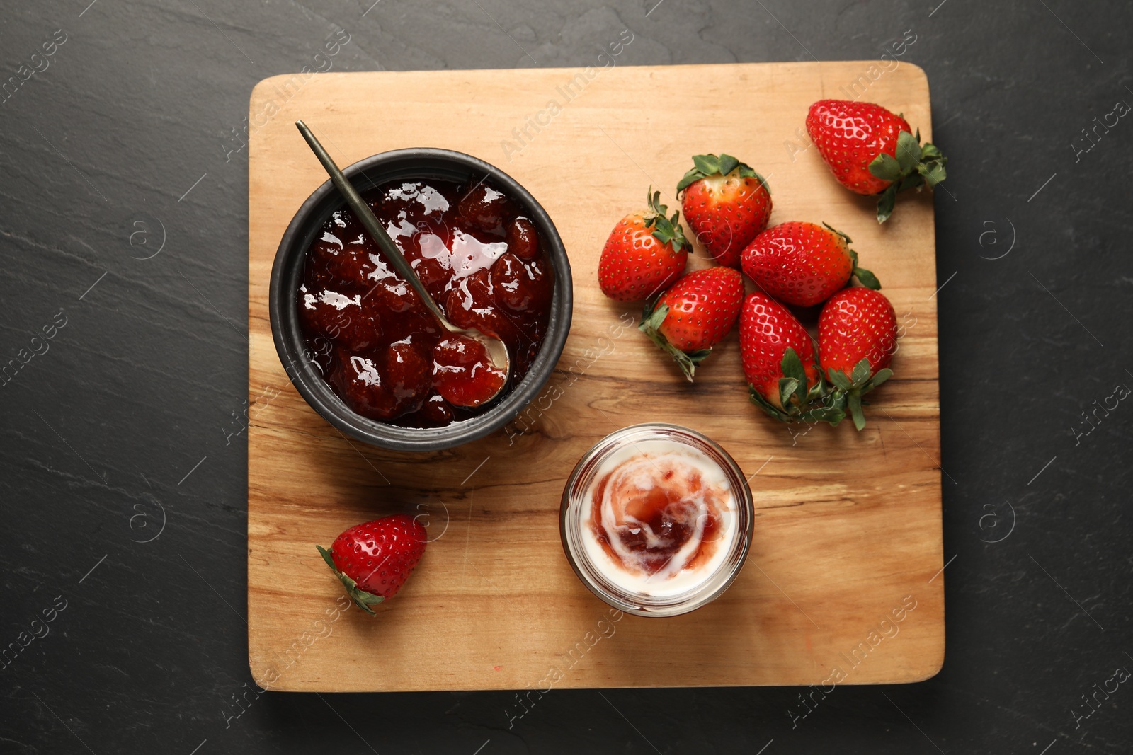 Photo of Tasty yoghurt with jam and strawberries on black table, top view