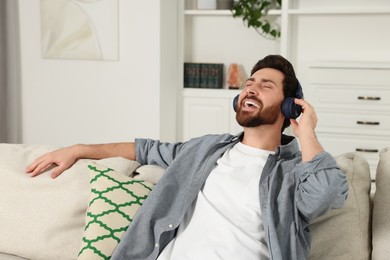 Happy man listening music with headphones on sofa indoors