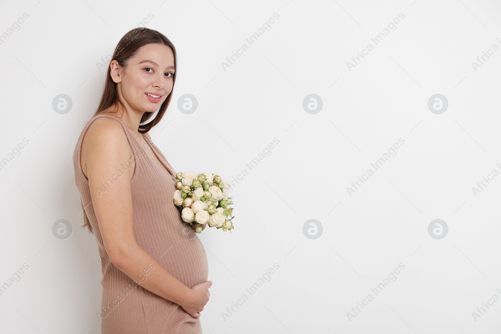 Photo of Beautiful pregnant woman in beige dress with bouquet of roses on white background, space for text