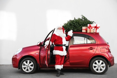 Photo of Authentic Santa Claus near red car with gift boxes and Christmas tree, outdoors