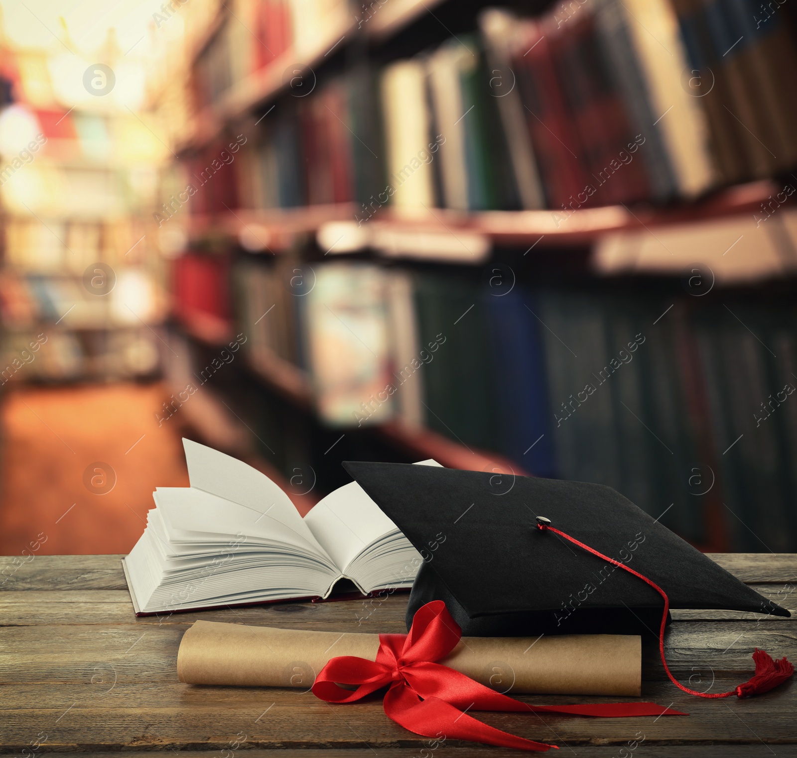 Image of Graduation hat, book and diploma on wooden table in library