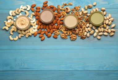 Different types of delicious nut butters and ingredients on light blue wooden table, flat lay. Space for text