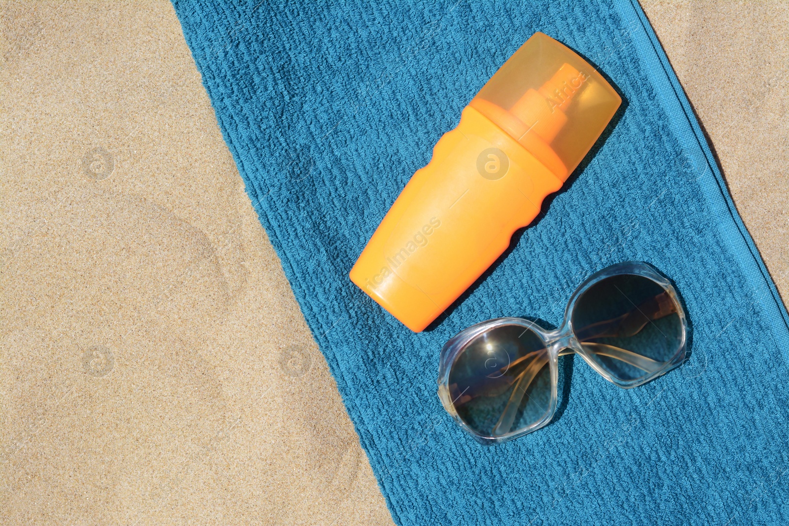 Photo of Soft blue beach towel with bottle of sunblock and sunglasses on sand, flat lay. Space for text