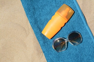 Photo of Soft blue beach towel with bottle of sunblock and sunglasses on sand, flat lay. Space for text