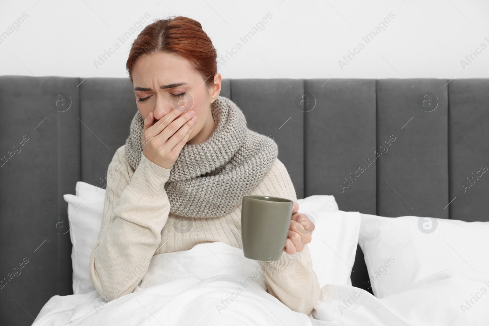 Photo of Woman with cup of drink and tissue coughing on bed, space for text. Cold symptoms