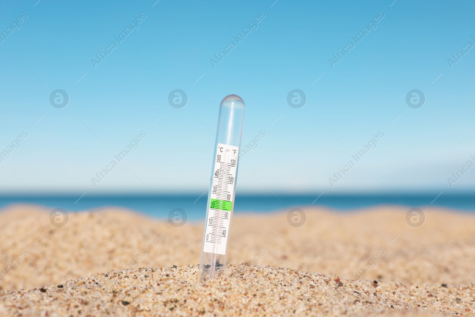 Photo of Glass weather thermometer in sand near sea