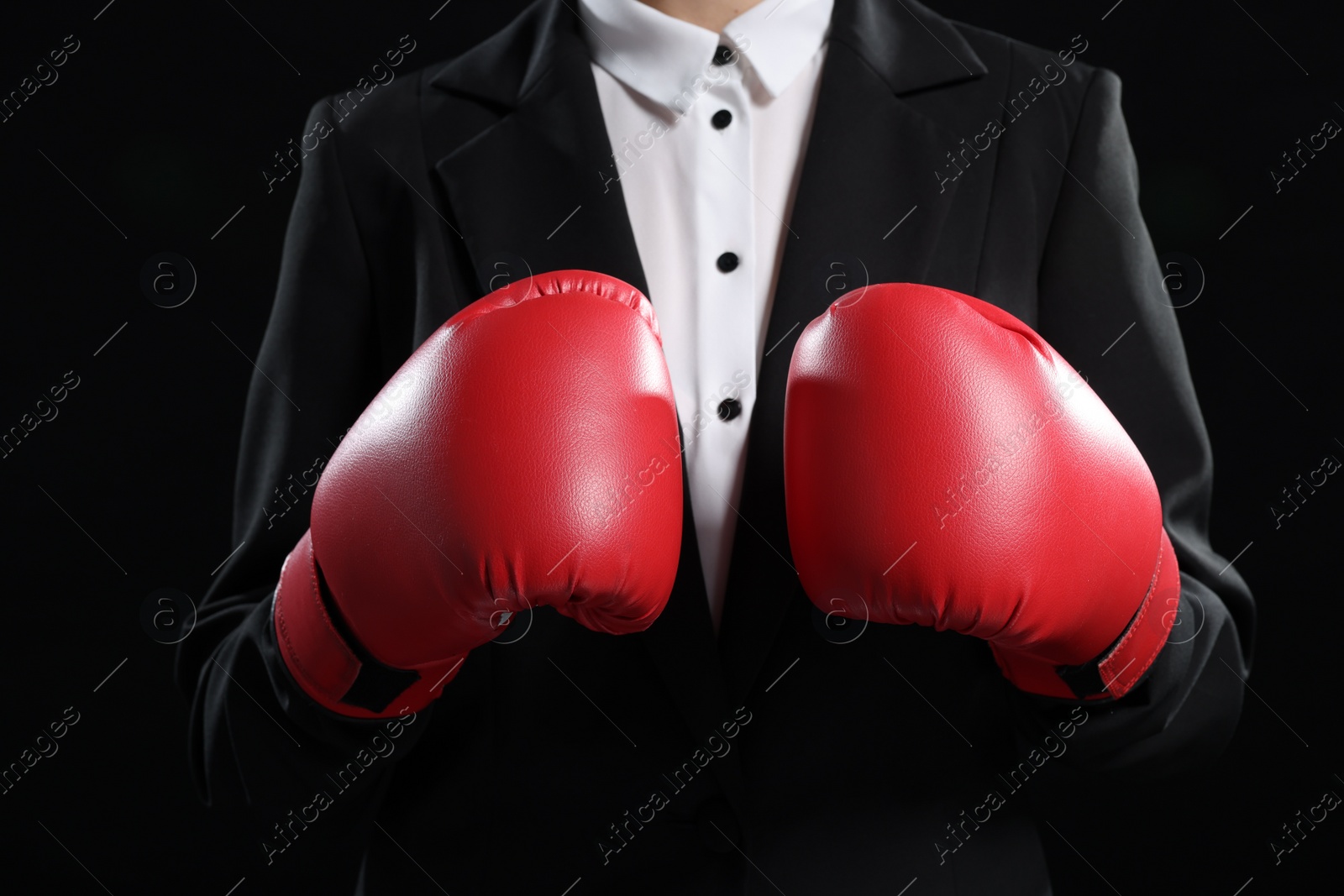 Photo of Businesswoman in suit wearing boxing gloves on black background, closeup