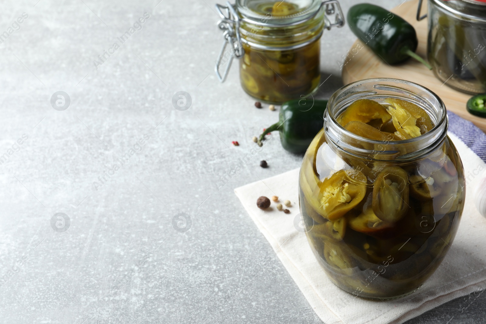 Photo of Glass jar with slices of pickled green jalapeno peppers on light grey table, space for text