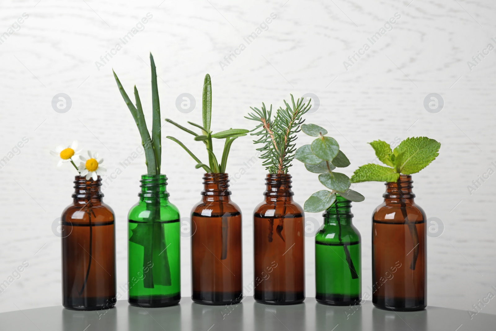 Photo of Glass bottles of different essential oils with plants on table