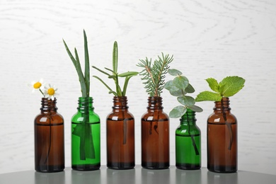 Photo of Glass bottles of different essential oils with plants on table