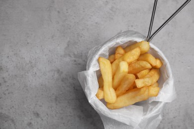 Photo of Frying basket with tasty french fries on light grey table, top view. Space for text