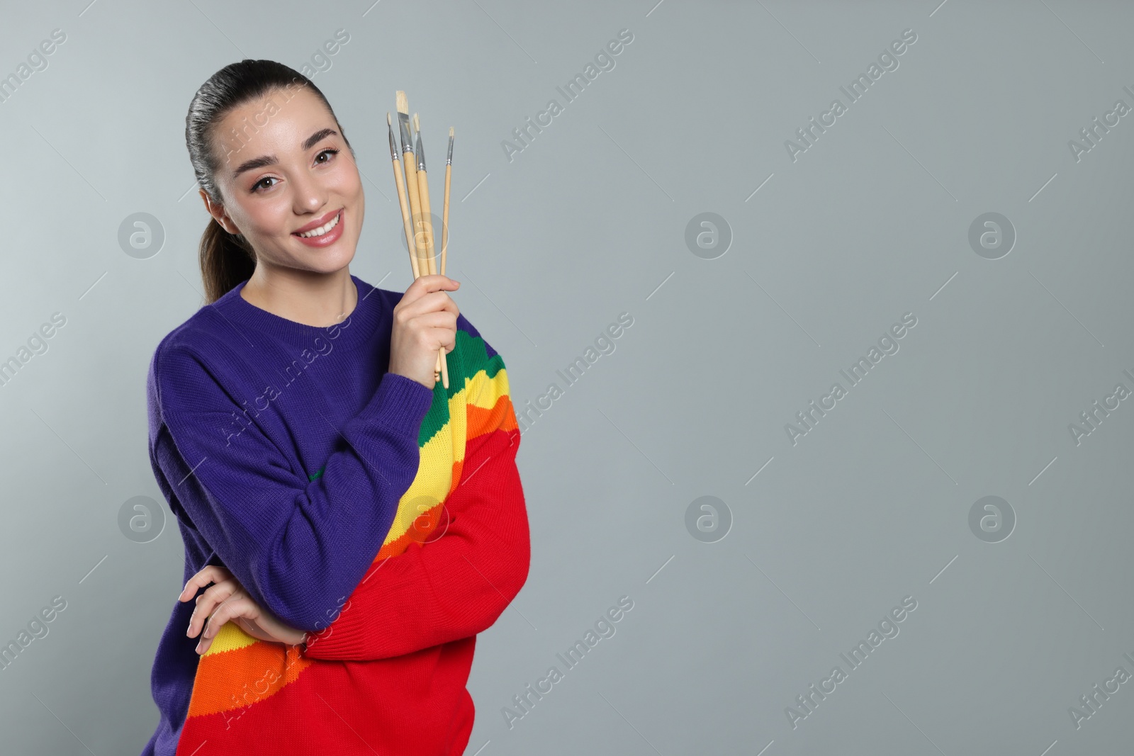 Photo of Woman with paintbrushes on grey background, space for text. Young artist