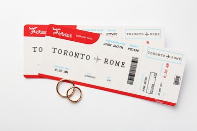 Photo of Honeymoon concept. Plane tickets and two golden rings on white background, top view
