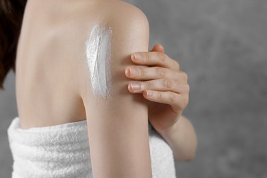 Woman applying body cream onto arm on grey background, closeup. Space for text