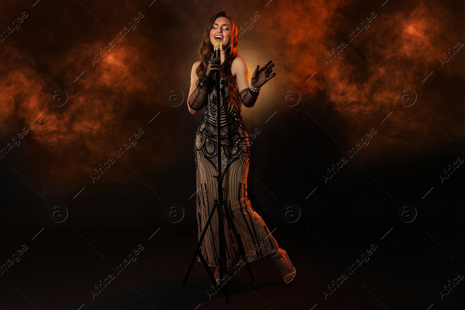 Photo of Beautiful young woman with microphone singing in color lights and smoke