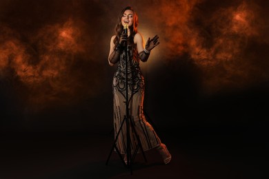 Photo of Beautiful young woman with microphone singing in color lights and smoke