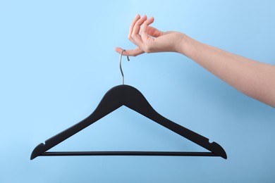 Photo of Woman holding hanger on light blue background, closeup