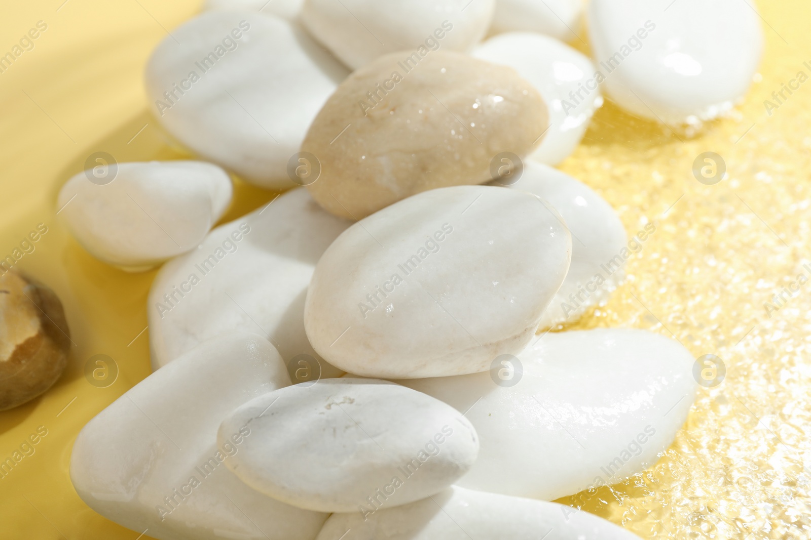 Photo of Spa stones in water on yellow background, closeup