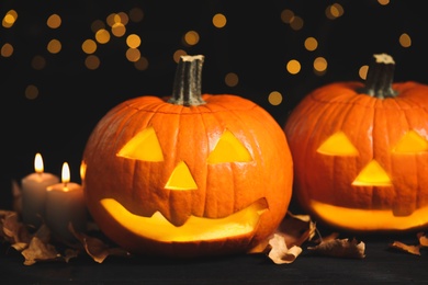Photo of Pumpkin jack o'lanterns, candles and autumn leaves on table against blurred background. Halloween decor