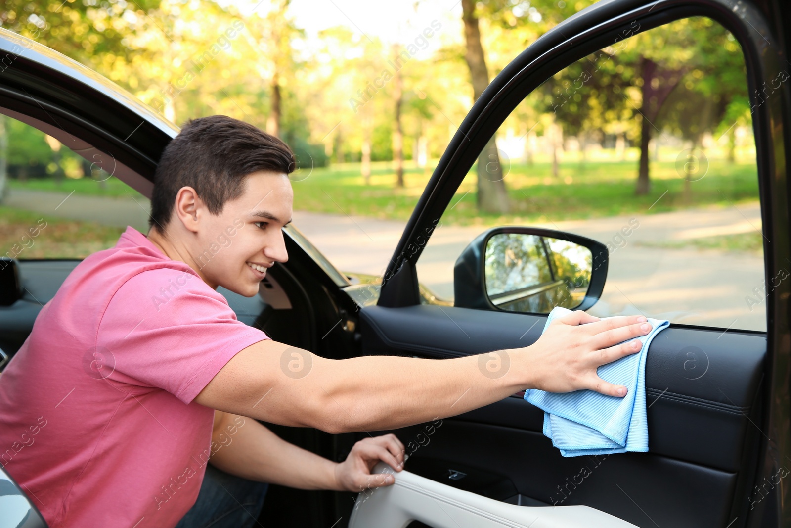 Photo of Young man washing car door with rag from inside