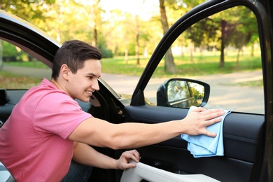 Young man washing car door with rag from inside