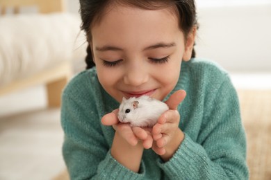 Photo of Little girl with cute hamster at home