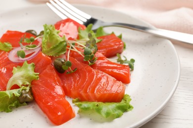 Photo of Salmon carpaccio with capers, lettuce, microgreens and onion on white wooden table, closeup