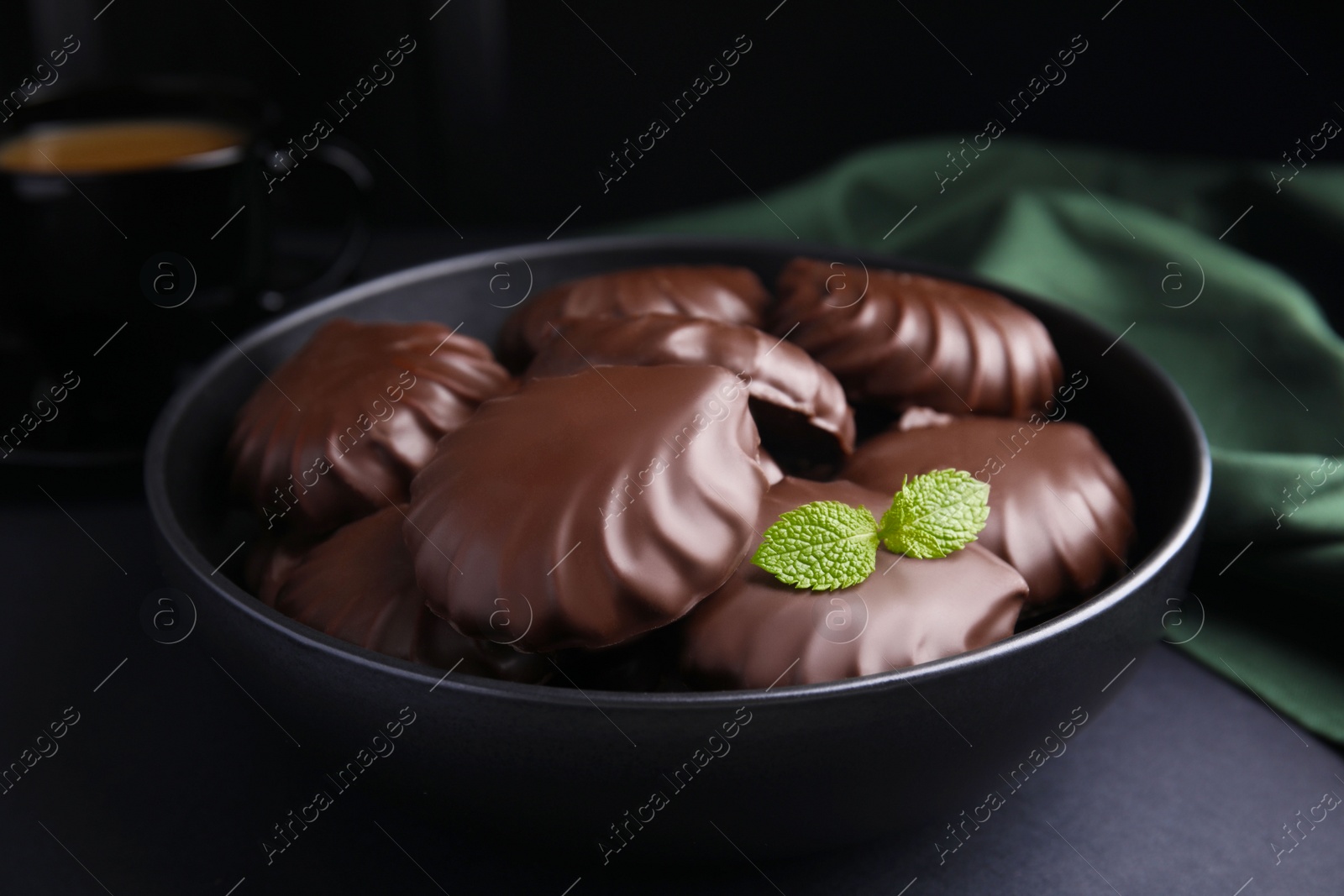 Photo of Delicious chocolate covered zephyrs with mint in bowl on black table, closeup