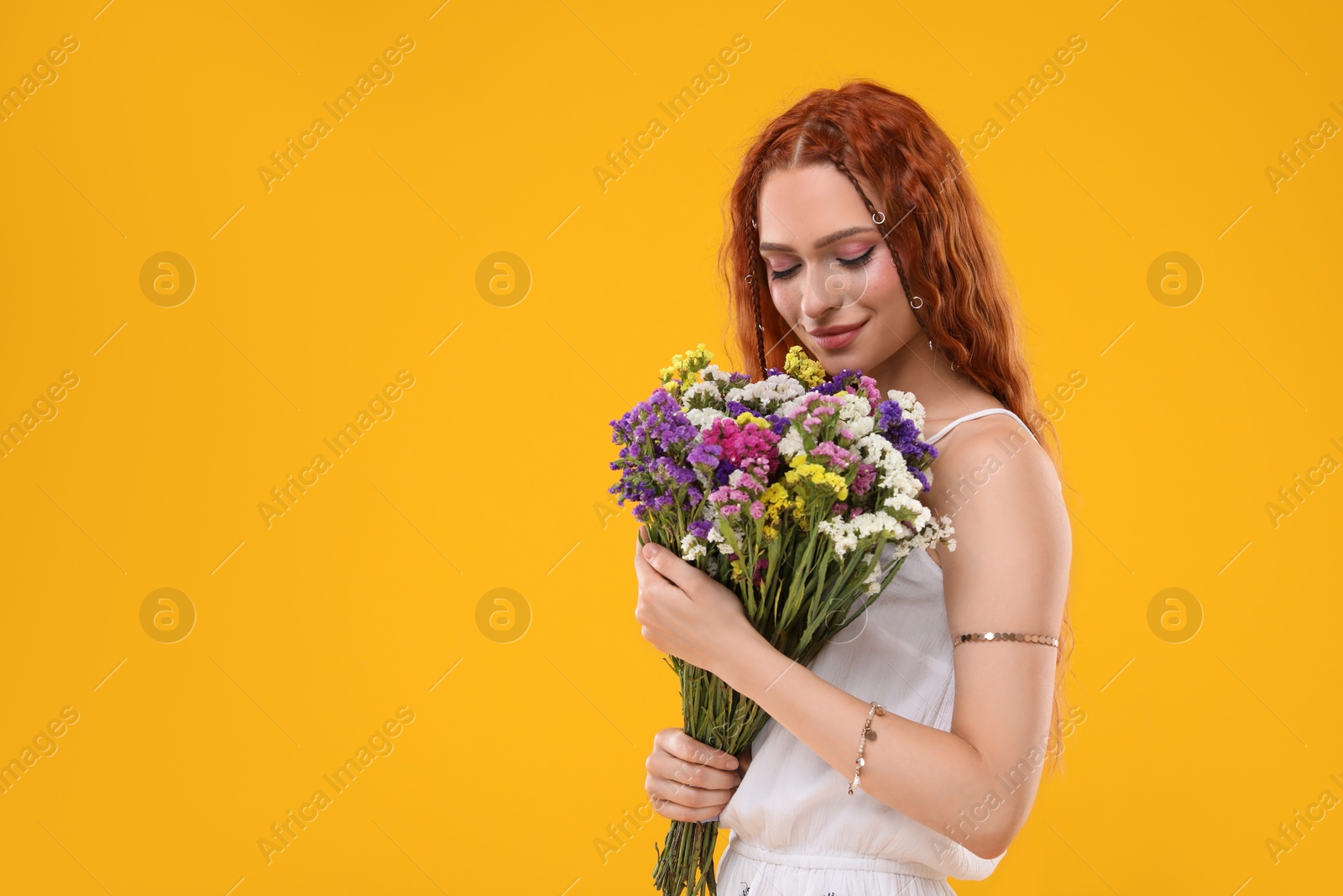 Photo of Beautiful young hippie woman with bouquet of colorful flowers on orange background, space for text