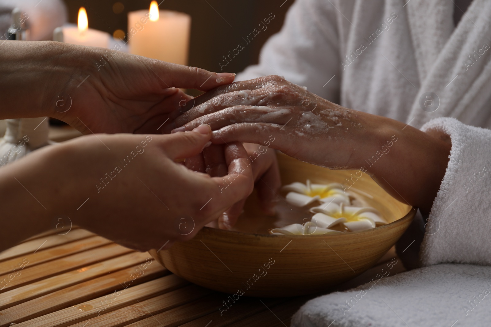 Photo of Woman receiving hand treatment at wooden table in spa, closeup