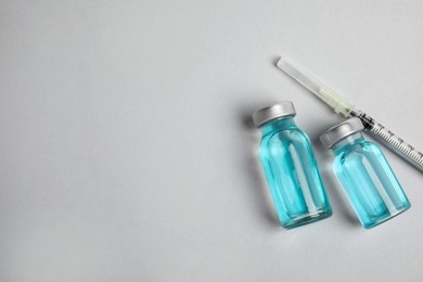 Photo of Vials and syringe on light background, flat lay with space for text. Vaccination and immunization