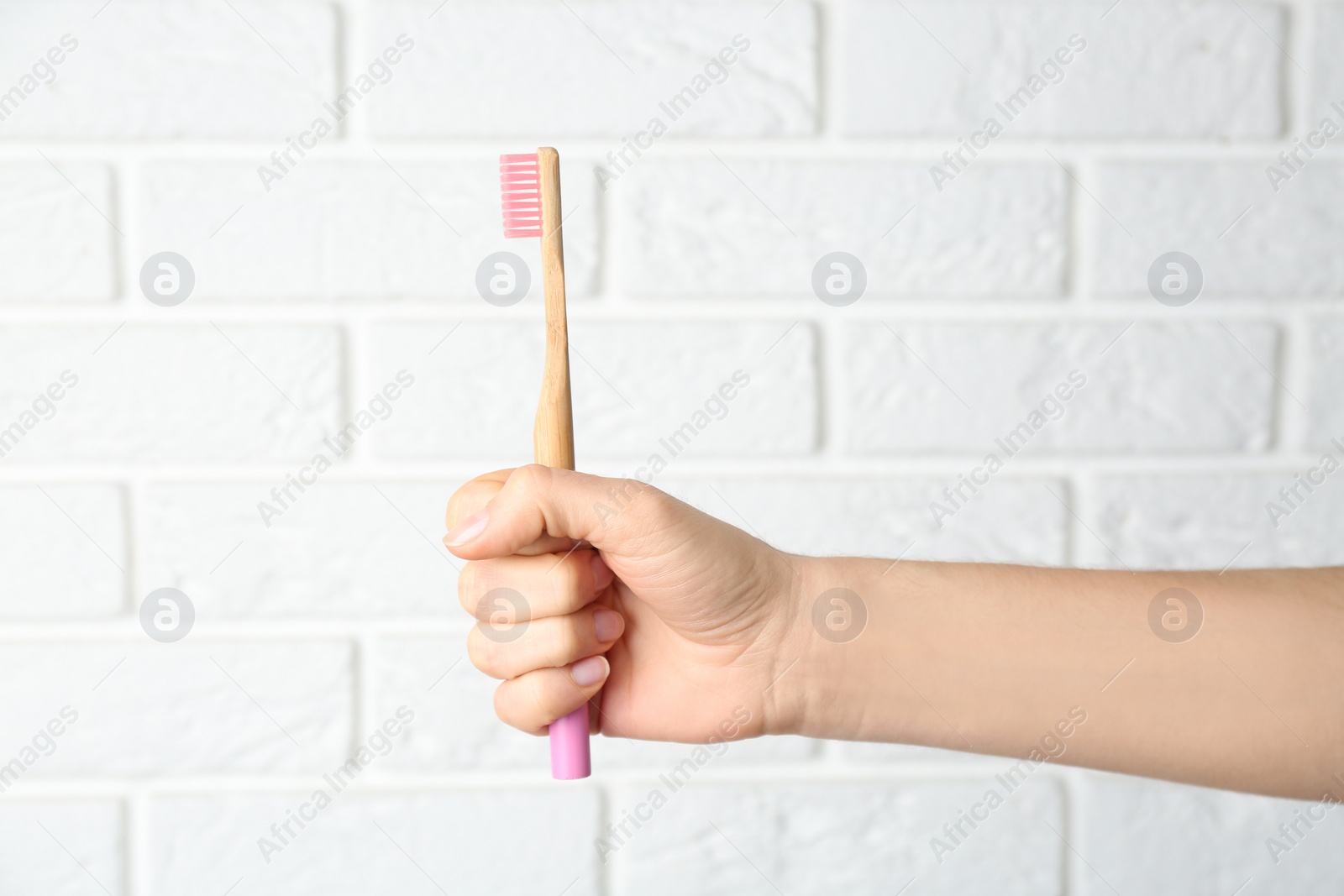 Photo of Woman holding bamboo toothbrush against white brick wall, closeup