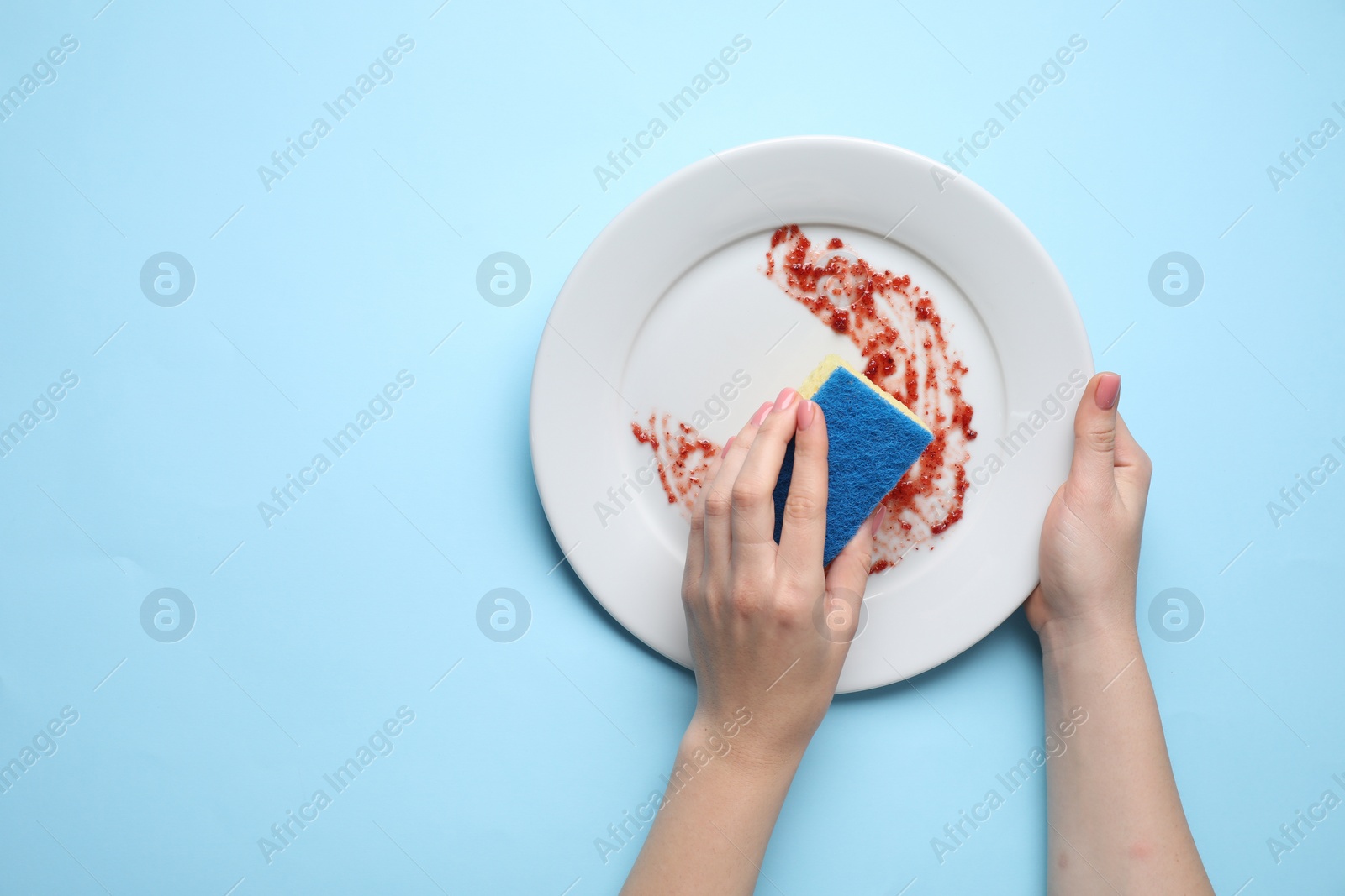 Photo of Woman washing dirty plate with sponge on light blue background, top view. Space for text