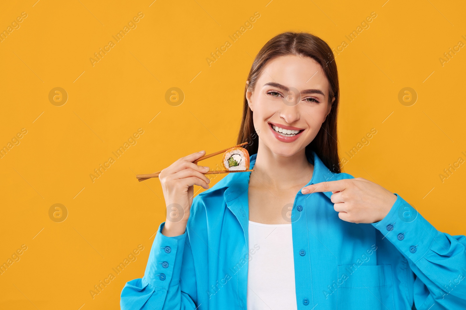 Photo of Happy beautiful young woman holding sushi roll with chopsticks on orange background. Space for text